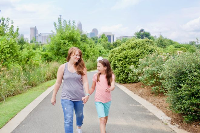 Women and young girl walking on city greenway holding hands