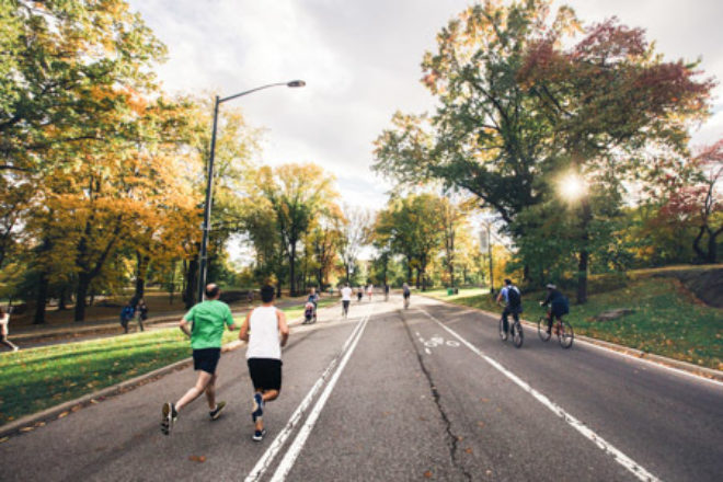 A man in a green shirt and a man in a white shirt running down the road together.